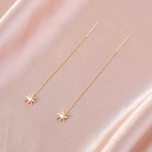 Detail of long gold star earrings with sparkling zircon on pink satin background