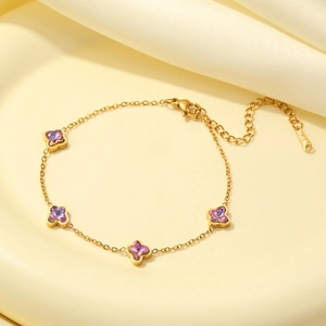 Elegant gold plated clover bracelet with purple zircon stones on a beige surface