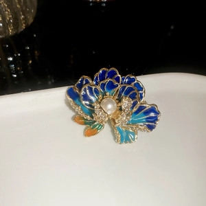 Macro detail of enamel flower brooch with pearl center and crystals on a white tray
