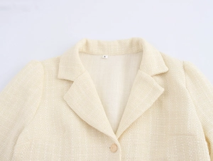 Dettaglio del colletto del blazer in tweed beige con bottone dorato e trama tessuta