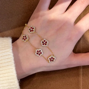 Detail view of five-flower gold bracelet with red stones worn on a person's wrist