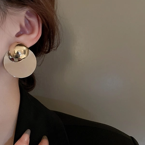 Close-up of minimalist gold geometric earrings on a model wearing a black blazer