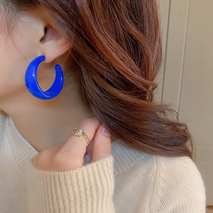 Close-up of model wearing vibrant blue C-shaped resin hoop earrings with glossy finish