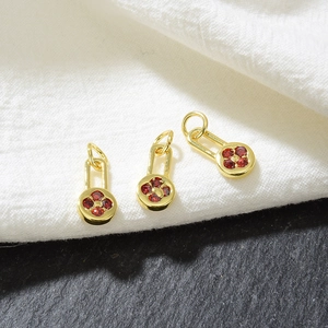 Macro shot of three golden rectangular charms with red floral zircon on a dark stone