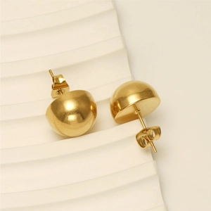 Close-up of golden polished dome earrings with butterfly backs on white textured backdrop
