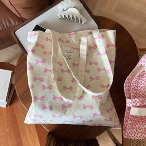Vue à plat d'un sac cabas en toile blanc cassé avec nœuds roses et petits pois bleus
