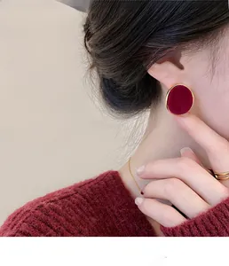 Close-up of burgundy flocked triangle stud earrings with gold trim on model wearing red sweater