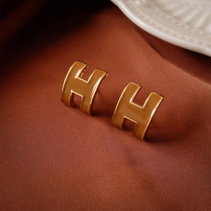 Detail of H-shaped enamel earrings in gold and caramel on a luxury silk background