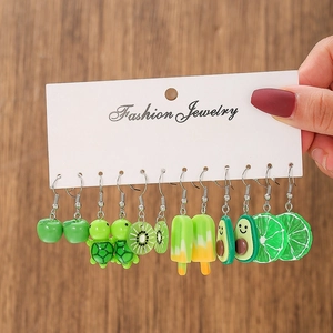 Main tenant une carte avec 6 paires de boucles d'oreilles en résine fruits et animaux