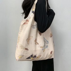 Detail view of large beige canvas tote bag featuring vintage butterfly prints on shoulder