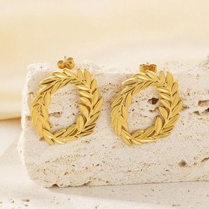 Macro shot of gold-plated leaf wreath earrings on a natural travertine stone surface