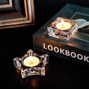 Star and square clear glass candle holders with burning tealights on a dark table