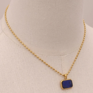 Detail of a gold chain necklace with a blue gemstone pendant on a mannequin bust