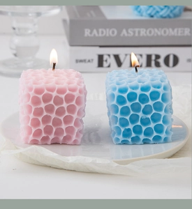 Pink and blue cube scented candles with honeycomb texture burning on a white tray