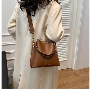 Brown bucket bag with wide strap styled with a beige coat in a minimalist indoor setting