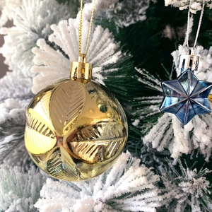 Close-up of golden textured ball and blue star ornaments hanging on a snowy Christmas tree