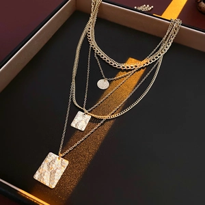 Detail of layered gold necklaces with hammered square and round pendants in a black box