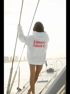 Λευκό oversized φούτερ με κόκκινο τύπωμα Amore στην πλάτη σε γιοτ στο ηλιοβασίλεμα