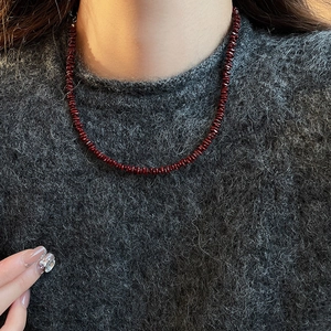 Detail of red garnet beaded necklace layered on a grey knit sweater for a vintage style