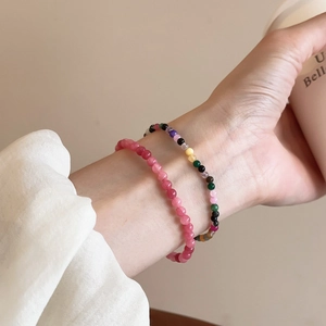 Hand mit rosa Erdbeerquarz-Perlen und bunten elastischen Armbändern im Boho-Stil