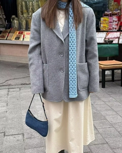 Detail shot of a grey wool blend coat featuring large patch pockets and a blue knit scarf