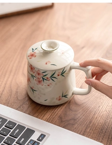 Detail of hand-painted peach blossom ceramic mug with lid on a wooden desk environment