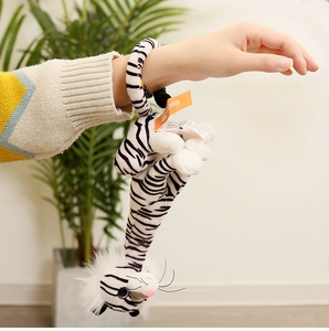 Close-up of a white plush tiger toy with black stripes worn on a wrist in nature