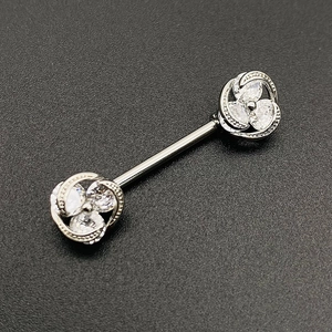 Macro shot of silver clover nipple ring with clear gemstones on textured background