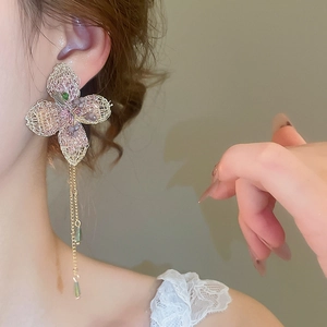 Dettaglio di orecchini a fiore rosa lavorati a maglia con nappe d'oro e perline
