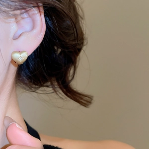 Close-up of golden brushed heart earring with star-set zircon on model's ear