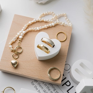 Golden rings and pearl necklace displayed on white heart and wood pedestals
