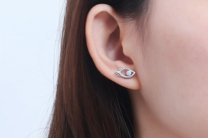 Close-up of a silver eye-shaped stud earring with eyelashes worn on a model's ear