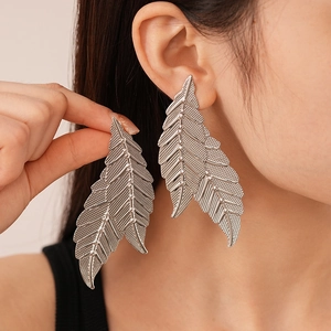 Detailed close-up of large metallic leaf-shaped earrings worn by a fashion model