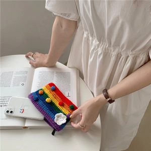 Close-up of rainbow crochet bag showing knit texture, zipper, and pom-poms