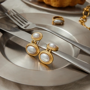 Elegant gold-plated pearl earrings and ring set displayed on a vintage plate