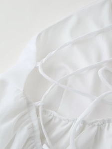 Detail of white backless mini dress featuring delicate criss-cross spaghetti straps and ruching