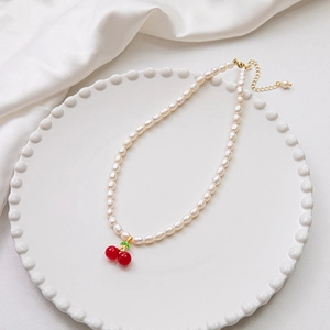 Freshwater pearl necklace with red cherry pendant on white ceramic plate