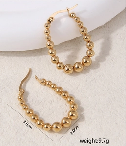 Macro detail of elegant gold-plated beaded oval hoop earrings with a high-shine mirror finish