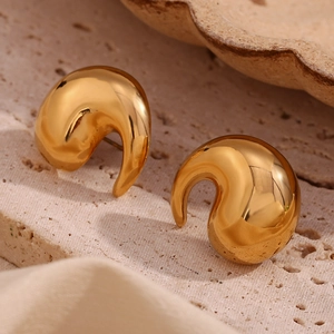 Detailed view of gold plated stainless steel swirl earrings on light brown stone background