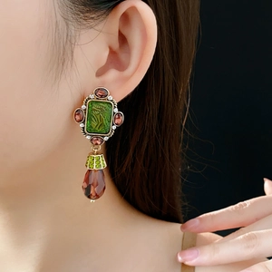 Close-up of vintage gold earrings with green relief stones and water-drop pendants on model