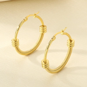Vue macro de boucles d'oreilles créoles dorées en acier avec texture spirale et perles empilées