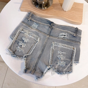 Dettaglio ravvicinato di shorts in denim usurati con tasche posteriori strappate e frange