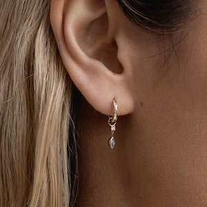 Close-up of a gold huggie hoop earring with marquise crystal charm on model