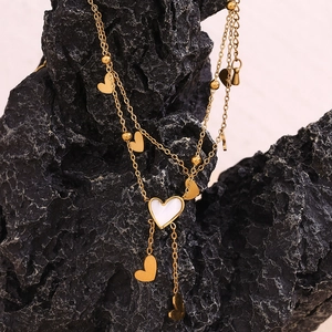 Detailed view of dual-layer gold anklet with white shell heart charms on black rock