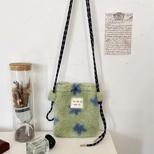Detail of plush green crossbody bag with blue floral pattern and woven strap