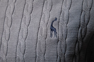 Close-up of grey knit sweater showing detailed cable texture and blue giraffe embroidery