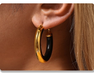 Close-up of chunky gold-plated stainless steel hoop earrings with black enamel inlay effect