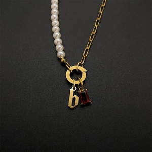 Detailed view of gold chain and pearl necklace with a red gem and letter pendant.