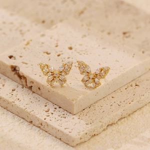 Detailed view of gold butterfly stud earrings with clear crystals on beige stone