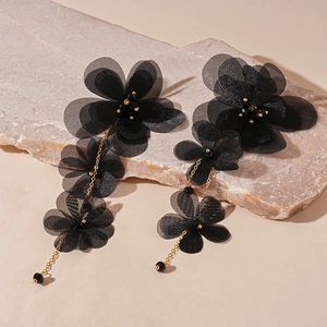Dettaglio macro dei raffinati orecchini a fiore in chiffon nero con catene di metallo d'oro